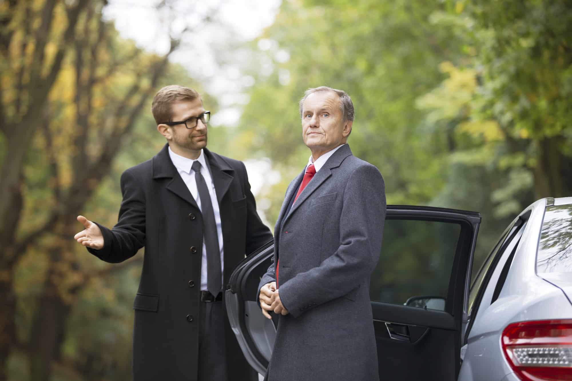 Chauffeur opening car door for businessman getting out